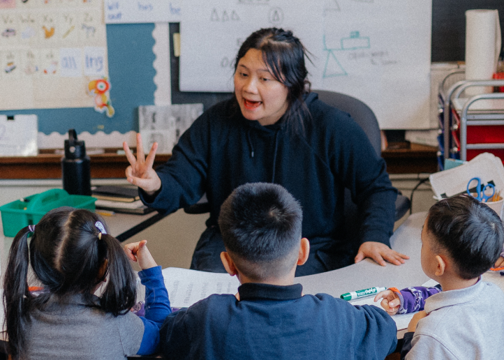 teacher instructing 3 students around a table