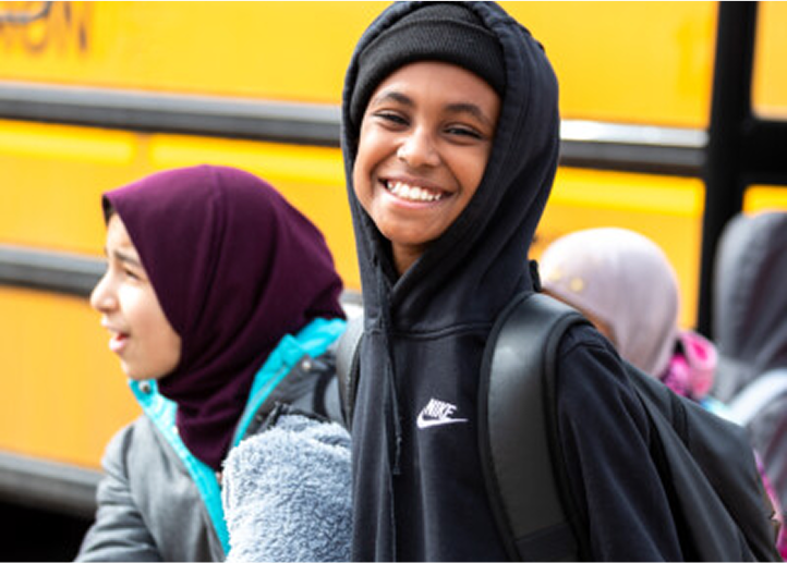 Smiling students getting off the school bus.